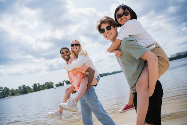 счастливые многоэтнические друзья в солнцезащитных очках, глядя в камеру, развлекаясь на пляже - Фото, изображение