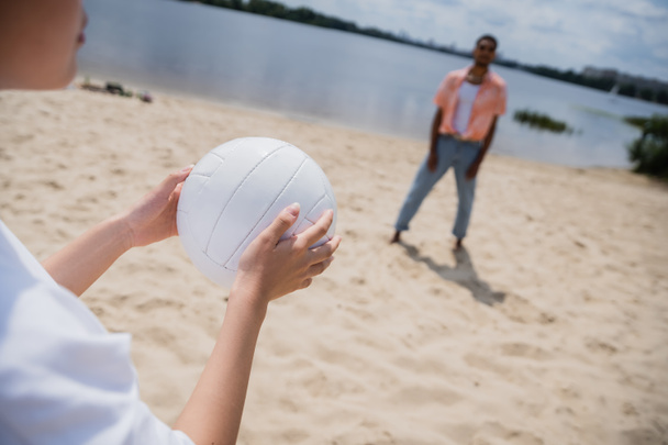 cropped view of woman holding ball near blurred african american man on riverside - Foto, imagen