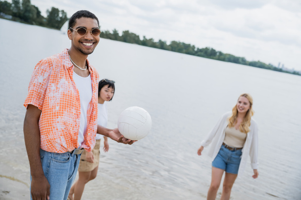 cheerful african american man with ball looking at camera near interracial women - Foto, Imagem