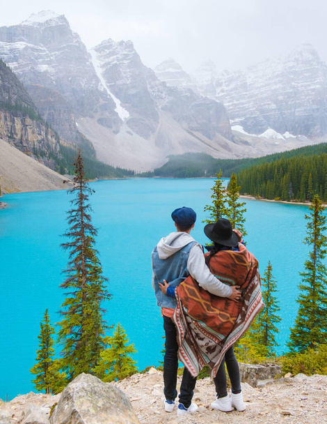  Lake moraine during a cold snowy day in Canada, turquoise waters of the Moraine lake with snow. Banff National Park of Canada Canadian Rockies. Young couple men and women standing by the lake - Zdjęcie, obraz