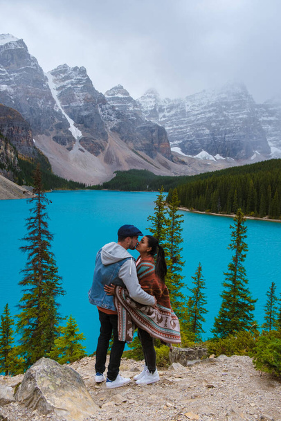  Lake moraine during a cold snowy day in Canada, turquoise waters of the Moraine lake with snow. Banff National Park of Canada Canadian Rockies. Young couple men and women standing by the lake - Foto, afbeelding