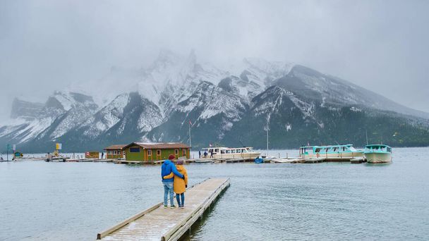 Minnewanka lake in the Canadian Rockies in Banff Alberta Canada with turquoise water, Lake Two Jack in the Rocky Mountains of Canada. a couple of men and women hiking by the lake during snow weather - Foto, imagen