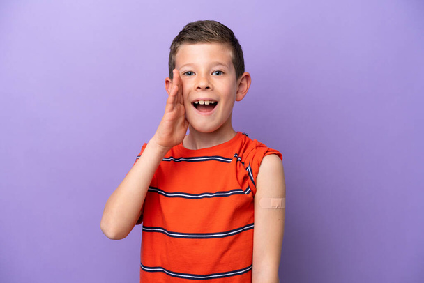 Little boy wearing a band aid isolated on purple background shouting with mouth wide open - Foto, imagen