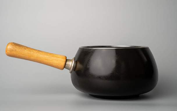 Dark gray cast iron frying pan or saucepan with wooden handle isolated on gray background. Stainless steel cooking pot. Saucepan, stewpan, kitchen utensils. Shiny deep frying pan. Fondue - 写真・画像
