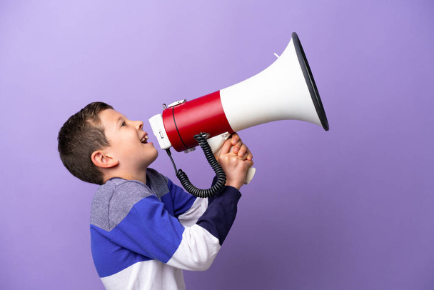 Маленький мальчик, изолированный на фиолетовом фоне, кричит через мегафон, чтобы объявить что-то в боковом положении - Фото, изображение