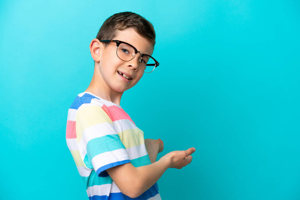 Little boy isolated on blue background With glasses and presenting something - Foto, Imagen