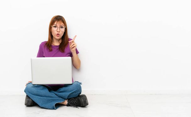 redhead girl with a laptop sitting on the floor intending to realizes the solution while lifting a finger up - Fotoğraf, Görsel