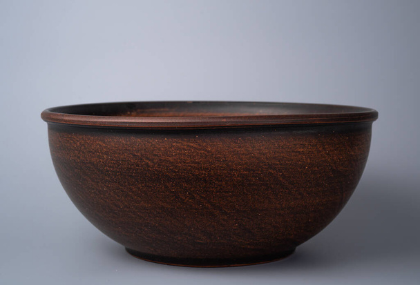 Empty earthen deep bowl on grey background. Brown handicraft ramekin. Empty earthenware, crockery from clay for food. Old dishes round shape - 写真・画像