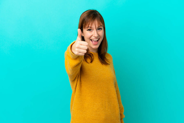 Redhead girl isolated on blue background with thumbs up because something good has happened - Foto, Imagen