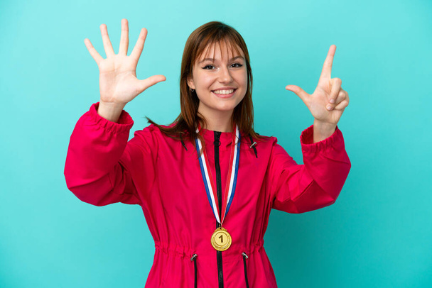 Redhead girl with medals isolated o blue background counting seven with fingers - Fotó, kép