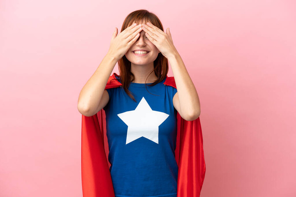 Super Hero redhead girl isolated on pink background covering eyes by hands - Φωτογραφία, εικόνα