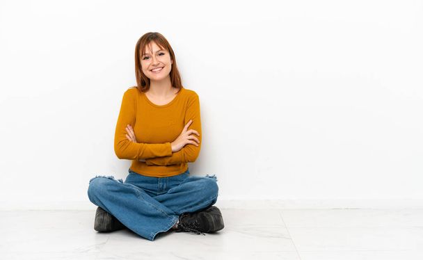 Redhead girl sitting on the floor isolated on white background keeping the arms crossed in frontal position - Foto, Bild