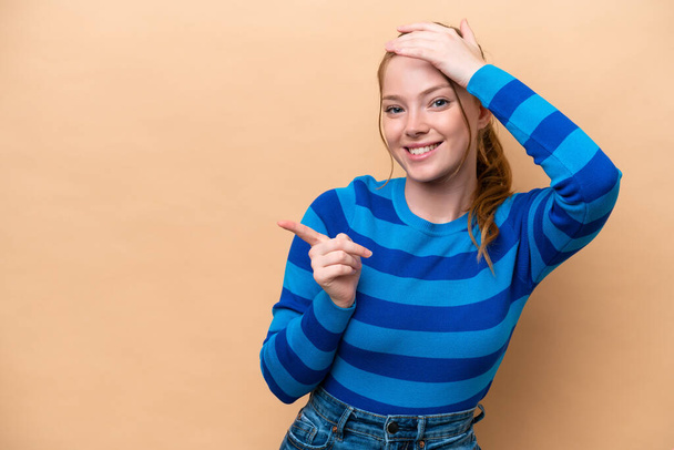 Young caucasian woman isolated on beige background surprised and pointing finger to the side - Photo, Image