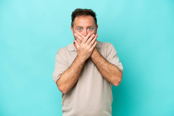 Middle age caucasian man isolated on blue background covering mouth with hands - Fotografie, Obrázek