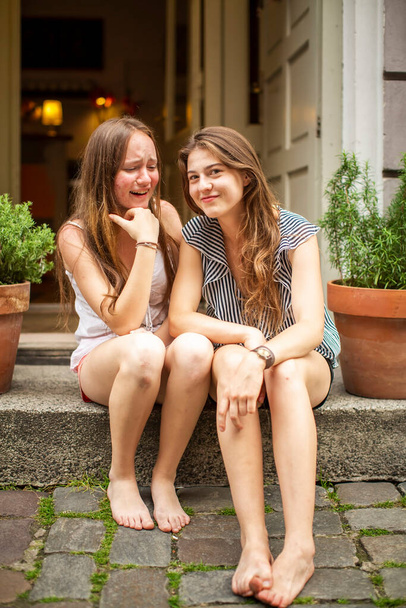 Two pretty girlfriends spend time on the stone steps of a house in the old town. - Fotó, kép