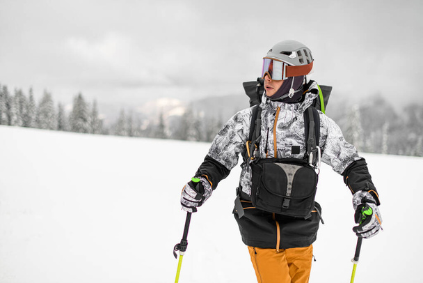 Male skier with ski suit and helmet and trekking poles on blurred winter landscape background - Foto, Imagem
