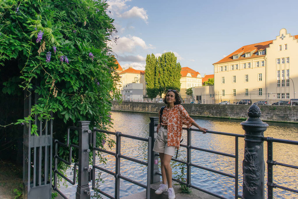 Кудрявая женщина в летнем наряде в полный рост стоит у реки в Берлине  - Фото, изображение