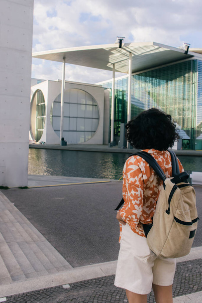 back view of curly young woman with backpack near modern contemporary building in berlin - Valokuva, kuva