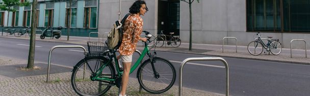 изумленная молодая женщина в летней одежде катается на велосипеде по улице в Берлине, баннер - Фото, изображение