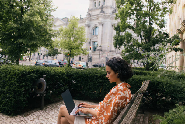 вид збоку молодого фрілансера, що сидить на лавці і використовує ноутбук у зеленому парку
  - Фото, зображення