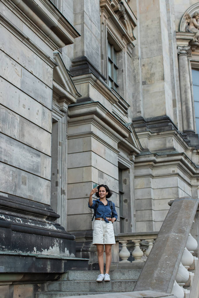 Счастливый турист в полный рост делает селфи на смартфон перед зданием в Берлине  - Фото, изображение