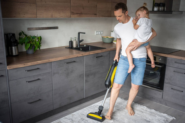 Father with his daughter on his hands vaccuming the floor in the modern home kitchen. High quality photo - 写真・画像