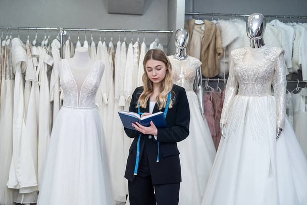 young female saleswoman holding a notebook and posing in a salon selling wedding dresses - Foto, Imagem