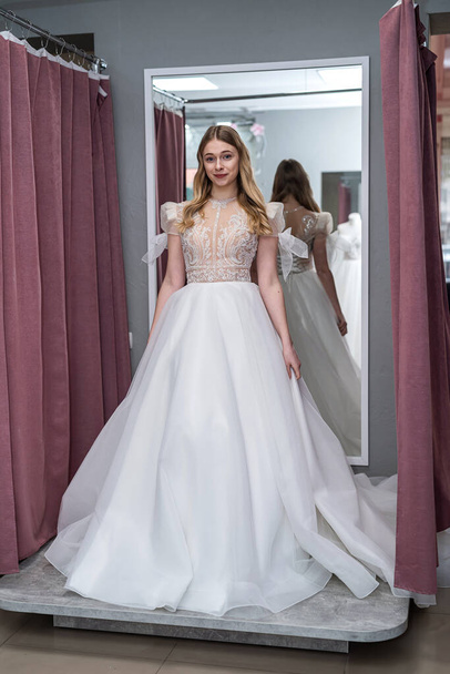 young prety woman is trying white wedding dresses in shop - Foto, afbeelding