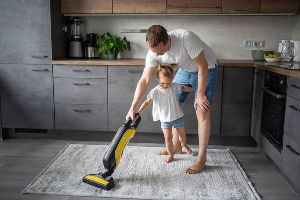 Father and daughter having fun with vacuum cleaner while cleaning at home kitchen. High quality photo - Photo, image