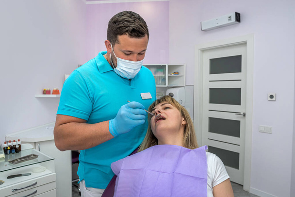 Όμορφος άντρας οδοντίατρος με μάσκα εξετάζει τα δόντια ενός ασθενή. Οδοντίατρος έννοια εξέταση αρσενικό - Φωτογραφία, εικόνα