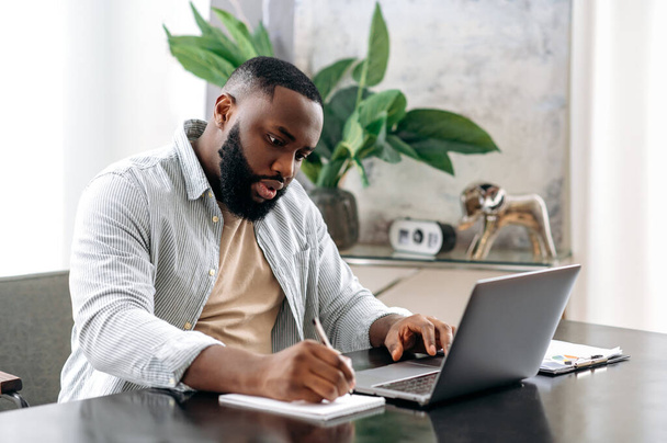 Орієнтований успішний розумний афроамериканський власник чоловічої компанії, менеджер, сидячи за столом в сучасному офісі, працюючи над проектом, з документами, аналізуючи, роблячи нотатки, готує звіт
 - Фото, зображення
