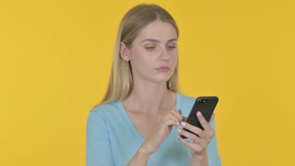 Casual απώλεια νεαρής γυναίκας στο Smartphone σε κίτρινο φόντο  - Πλάνα, βίντεο