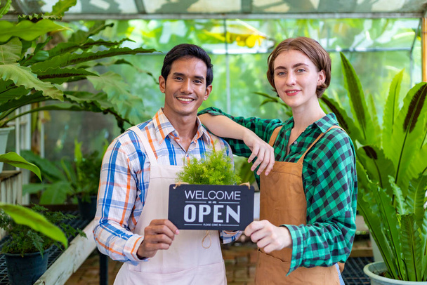 Team of diversity garden workers holding opening sign to welcome customer to their tropical nursery plant center full of exotic fern species  - Φωτογραφία, εικόνα