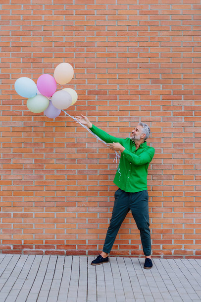 A fun portrait of happy energetic mature businessman holding balloons in street, feeling free, work life balance concept. - Fotoğraf, Görsel