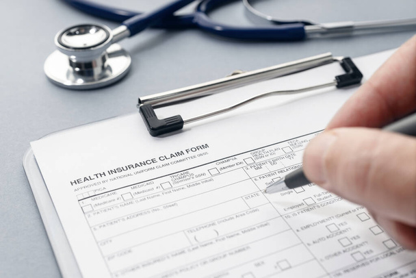 Hand filling on Health Insurance claim form and stethoscope on desk - Foto, immagini
