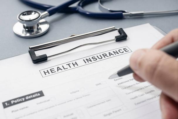 Hand writing on Health Insurance form and stethoscope on desk - Photo, image