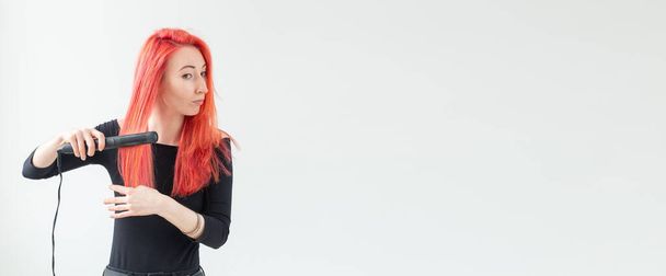 Coiffure, coiffeur et concept de personnes - élégante femme aux cheveux roux avec fer à friser sur fond blanc
 - Photo, image