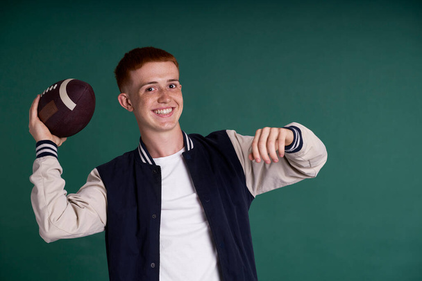 Successful red head boy holding American football ball and looking at camera - Photo, Image