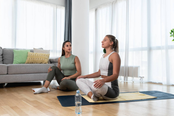 Young fitness and yoga instructor working in your home. Sporty educated woman helping young girl at her apartment at in home workout and training for healthy life.  - 写真・画像