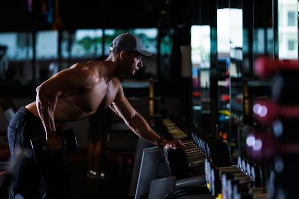 μυώδης άνδρας γυμνάζεται με αλτήρες στο γυμναστήριο σκούρο τόνο,  - Φωτογραφία, εικόνα