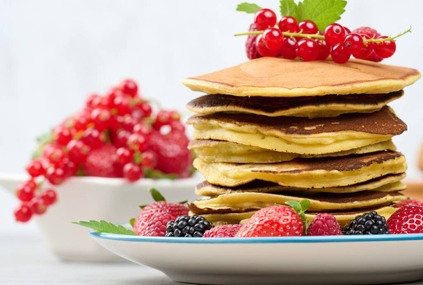 Stack of baked pancakes with fruits in a round plate on a white table - Foto, afbeelding