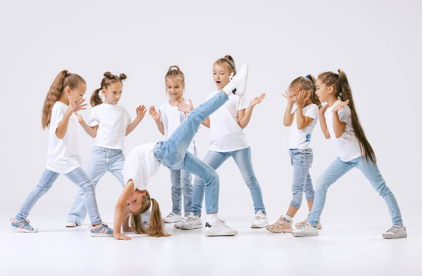 Joy, fun and happiness. Portrait of happy, active little girls, sportive kids in casual clothes dancing isolated on white studio background. Concept of music, fashion, art, childhood, hobby. - Фото, изображение