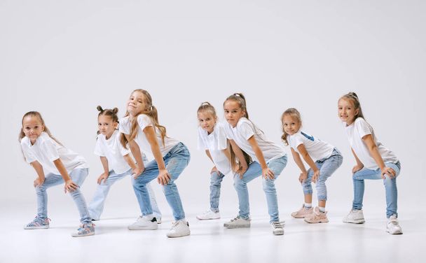 Joy, fun and happiness. Portrait of happy, active little girls, sportive kids in casual clothes dancing isolated on white studio background. Concept of music, fashion, art, childhood, hobby. - Fotoğraf, Görsel