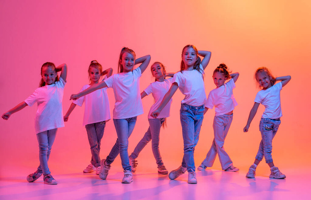 Hip-hop dance, street style. Group of children, school age girls in casual style clothes dancing in choreography class isolated on pink background in yellow neon light. Concept of music, fashion, art - Foto, Bild