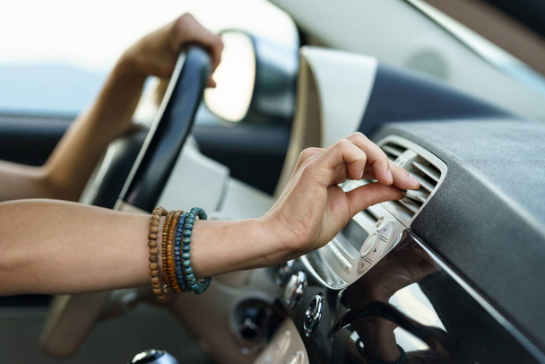 Driver goes on road trip sitting at steering wheel and driving in rural area on hot summer day. Woman puts hand on modern panel vent to check cold air flow and operation of ventilation system closeup - Φωτογραφία, εικόνα