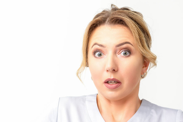 Female doctor shocked. Close up portrait of a young caucasian woman looking surprised with wide eyes stared isolated white wall background - Fotó, kép