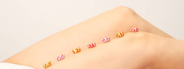 Depilation, waxing concept. Round candies lying down in a row on the female leg, close up - Photo, image
