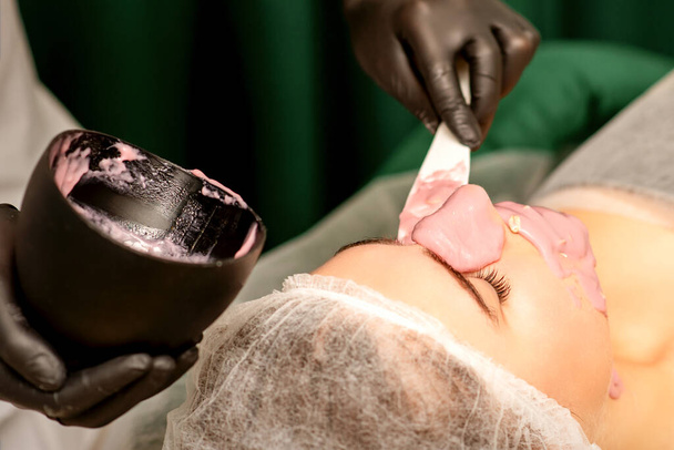Beautiful young caucasian woman receiving an alginic mask to the face in beauty salon. Facial skin treatment - Zdjęcie, obraz