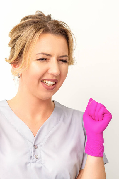 Счастливая белая женщина врач в розовых перчатках празднует и поднимает кулаки на белом фоне - Фото, изображение