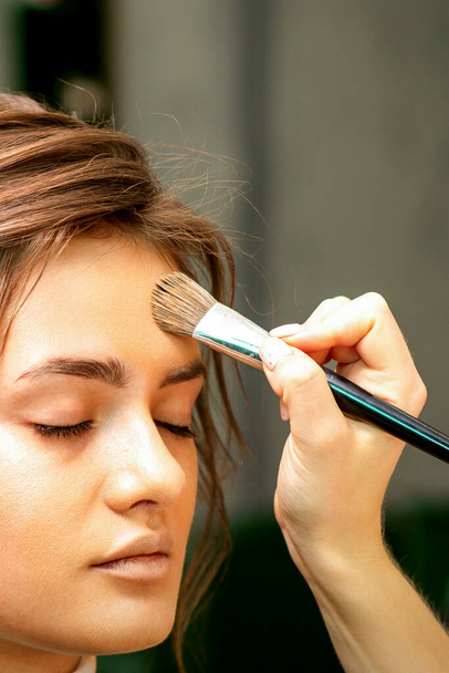 The makeup artist applies a cosmetic tonal foundation on the face using a makeup brush - Photo, image